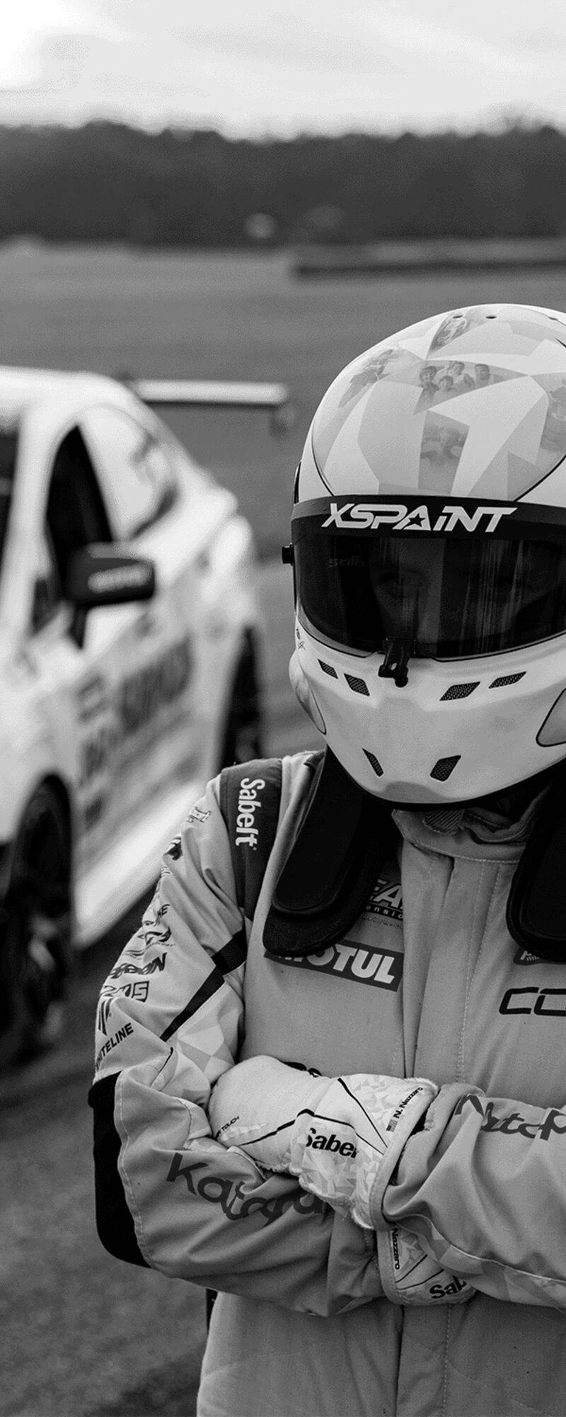 Nicholas Nazzaro wearing a helmet and race suit beside a Subaru race car.