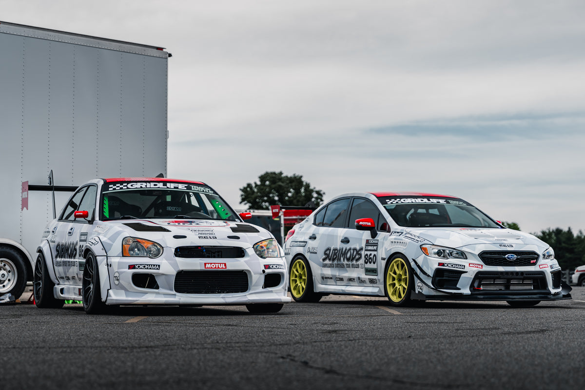 The white Subimods and EFI Performance number 861 and number 860 Subaru WRX STI race cars together in the paddock.