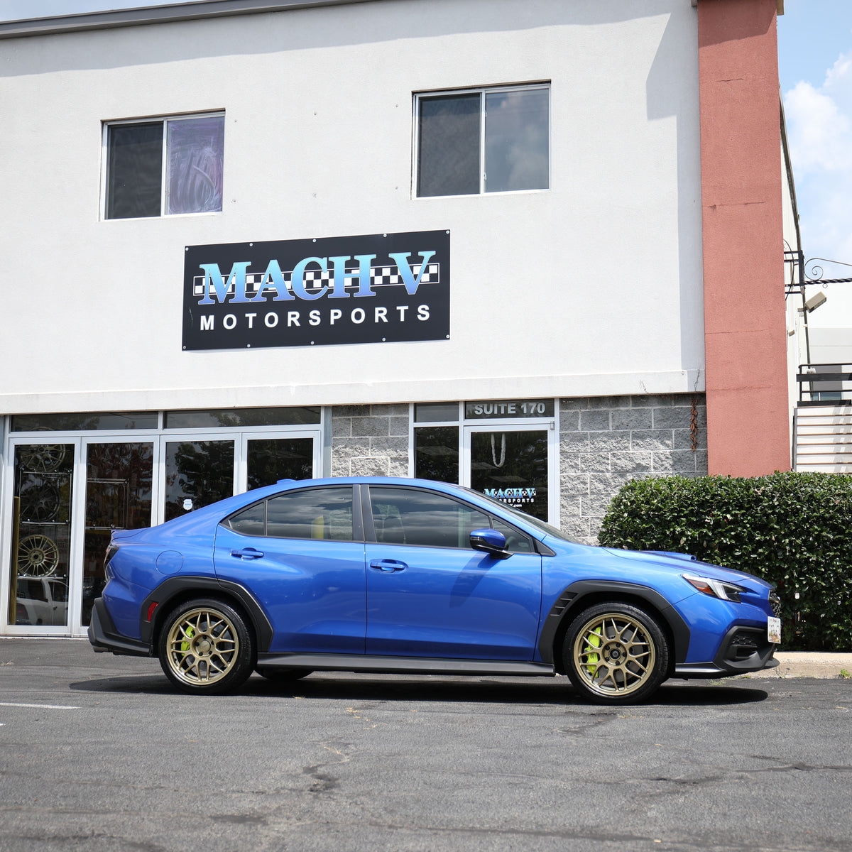 A blue Subaru WRX parked outside the Mach V Motorsports storefront.